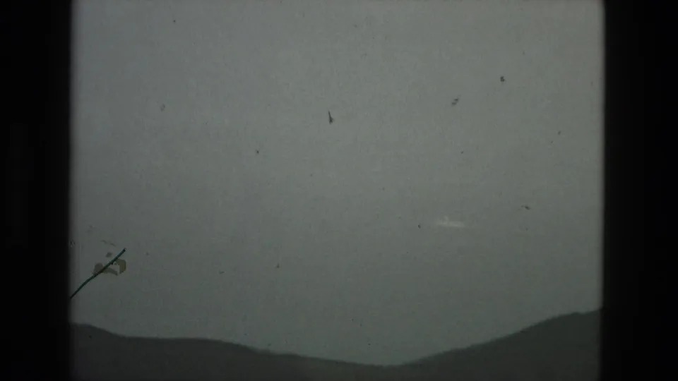 1978 Granada 8mm frame with a dark hill line under clouded sky, interrupted by a visible scratch and central film-gate border.