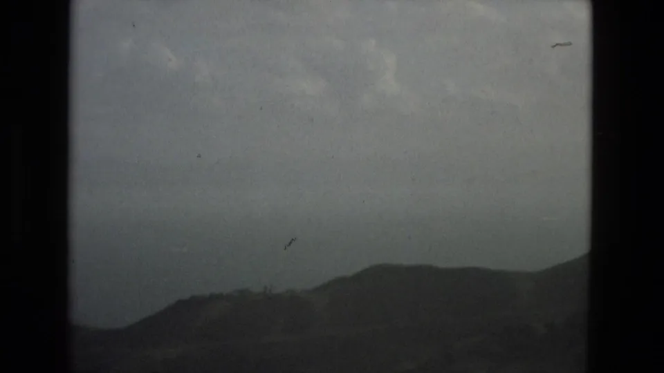 1978 Granada 8mm frame showing a dark mountain ridge under mottled grey clouds, with pronounced grain, scratches, and film-frame borders.