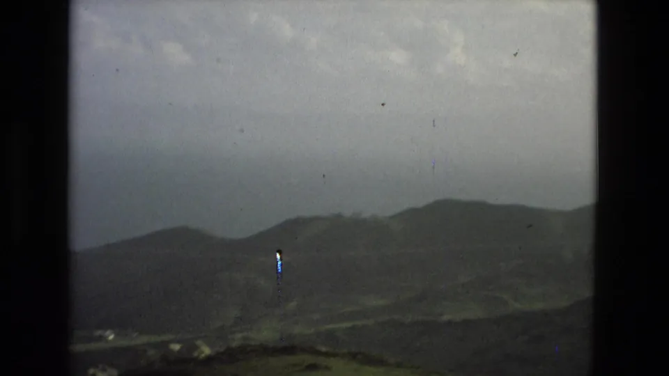 Granada-area landscape view on faded 8mm film, with low hills, cloudy sky, and visible gate edges.
