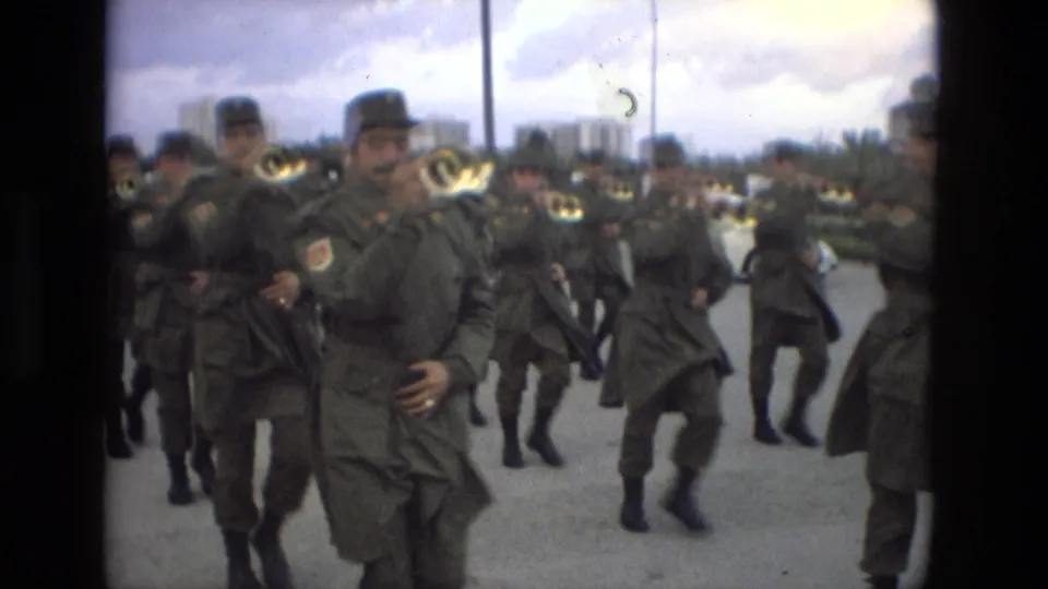 Olive-uniformed military band members march toward the camera in Granada, Spain, playing brass horns during a public parade.