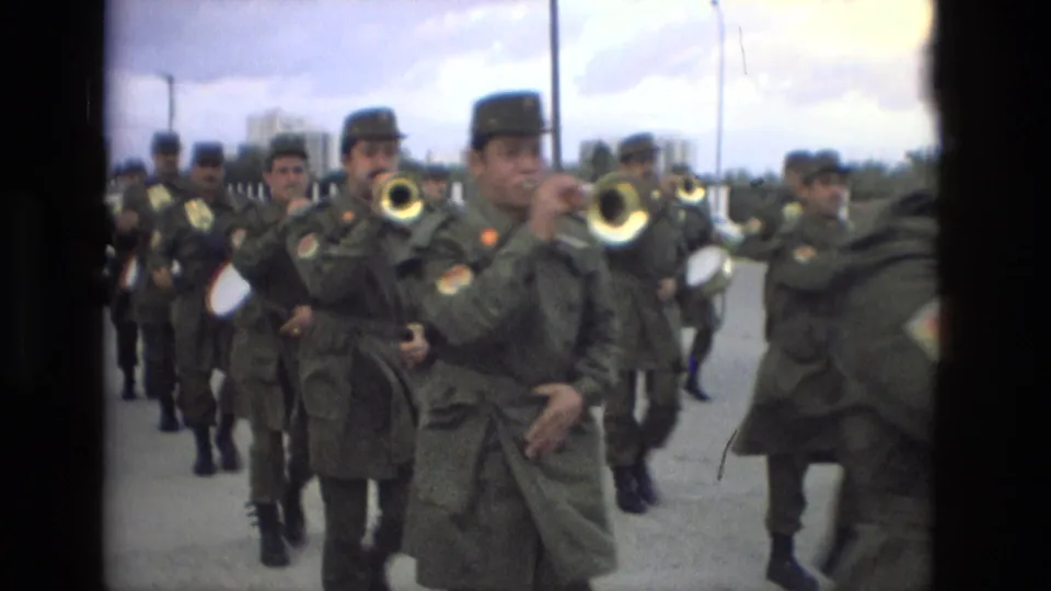 Close 8mm view of uniformed brass players marching in Granada, Spain, with soldiers and drums visible behind them.
