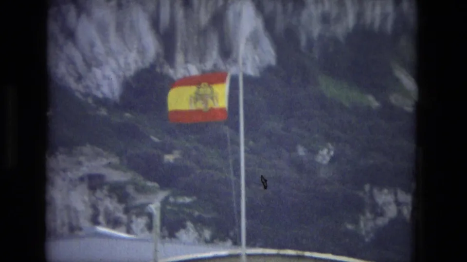 A Spanish flag on a flagpole is filmed against rocky terrain, matching the supplied Cordoba, Spain clip context.