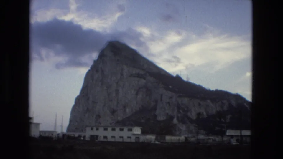 1978 Spain 8mm frame of a rocky landmark seen from across low buildings, with visible grain and soft exposure.