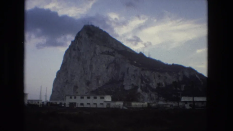 1978 Spain 8mm view of the rocky landmark from a distance, with low buildings and a dark foreground strip.