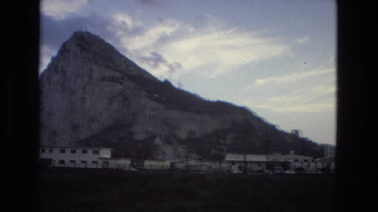 Rocky mountain rising behind low buildings under a cloudy sky.