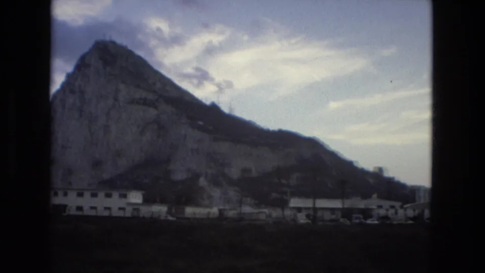 1978 8mm frame showing a large rocky mountain above low buildings in the Spain location identified by the clip metadata.