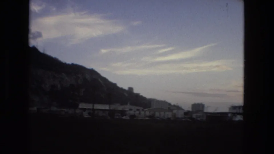 1978 8mm frame with a shadowed mountain slope, low city buildings, and streaked clouds over the Spanish location noted in metadata.