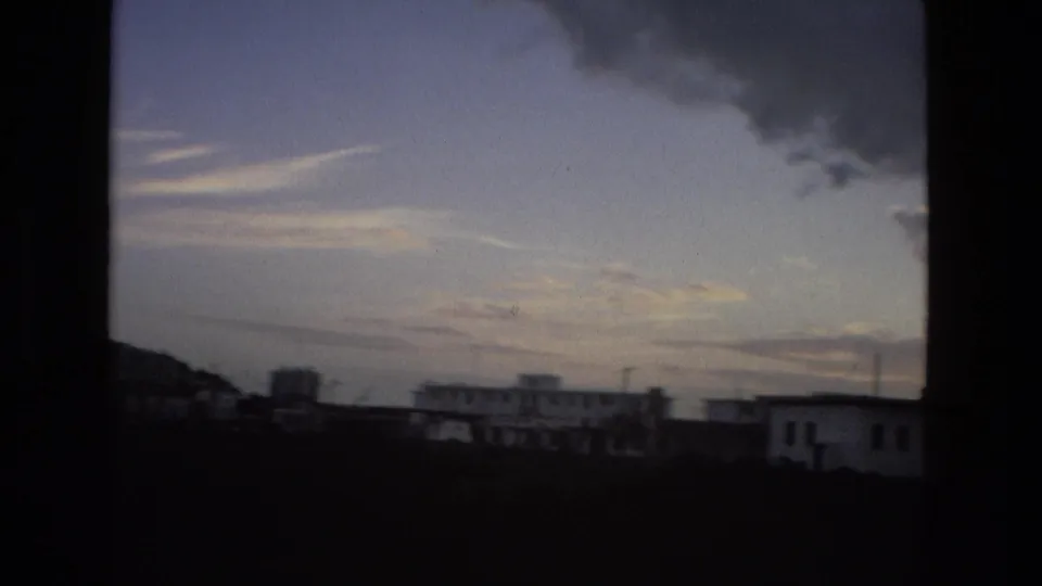 1978 8mm frame looking across low buildings, open land, and a broad evening sky in the Spanish city setting from the clip metadata.