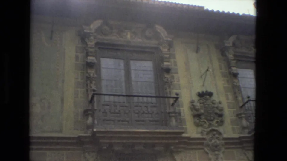 A yellow-beige Córdoba facade shows carved ornament, a shuttered window, and a small wrought balcony in soft 8mm color.