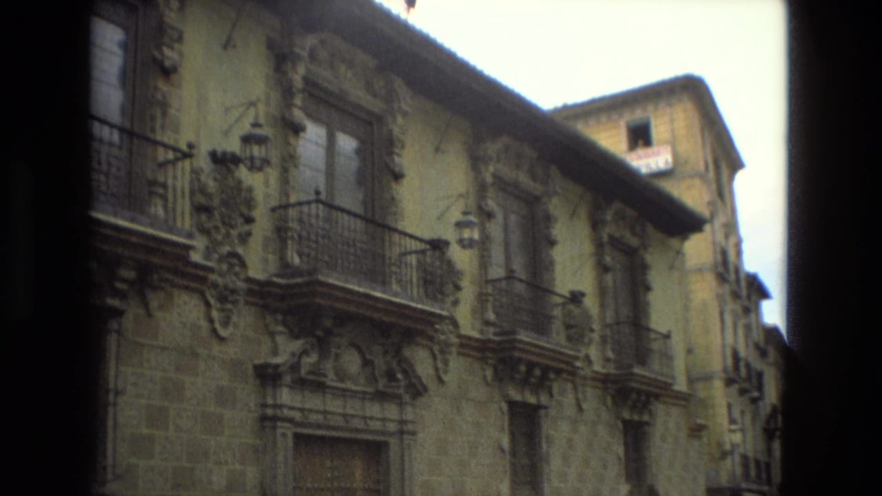 Narrow historic street with ornate stone facades, iron balconies, and dark film gate edges.