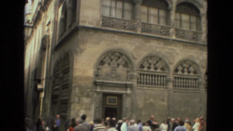 A group of tourists stands near a Córdoba stone facade with arched windows, a carved doorway, and upper-level ironwork.