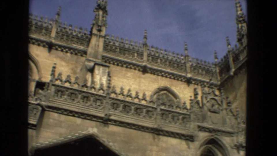 1978 Córdoba home-movie frame of an upper religious facade with spires, carved balustrade, and blue sky.