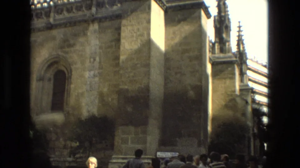 1978 Cordoba home-movie view down a narrow exterior space beside a historic stone church wall with an arched window and upper spires.