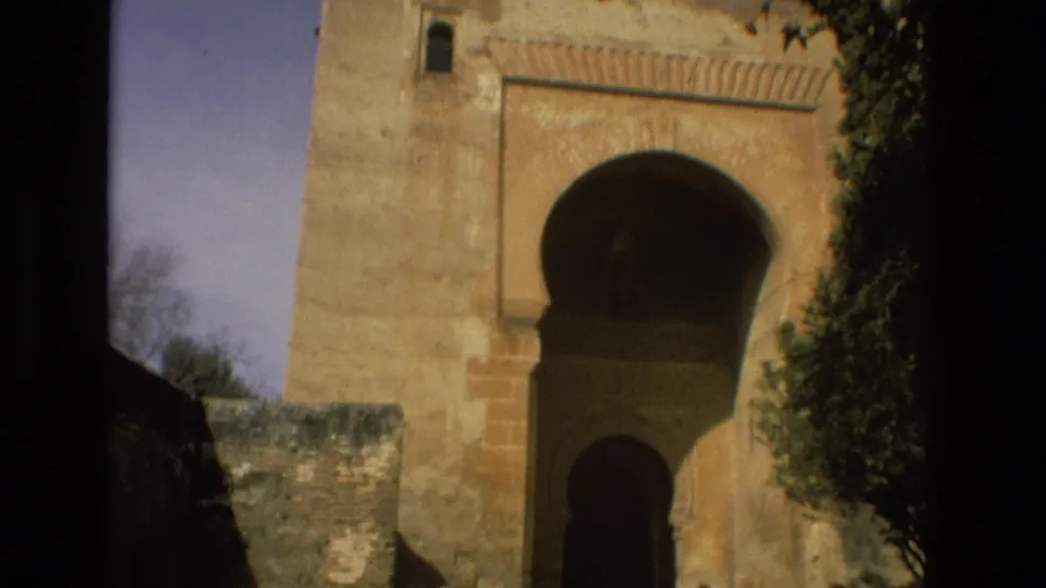Córdoba, Spain, 1978 home-movie frame of a weathered stone building with arched openings and surrounding greenery.