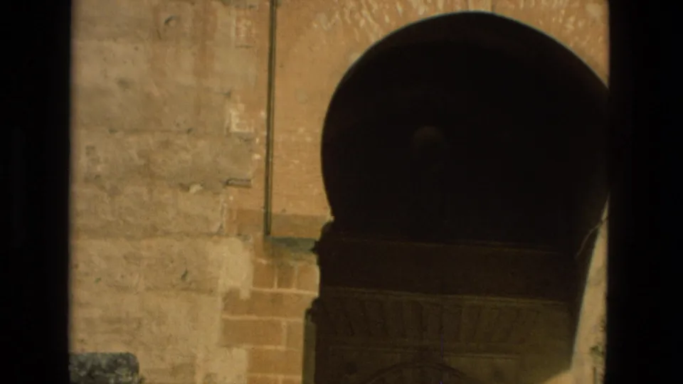 1978 Córdoba home-movie frame showing a sunlit stone facade with a shadowed horseshoe arch and weathered masonry.
