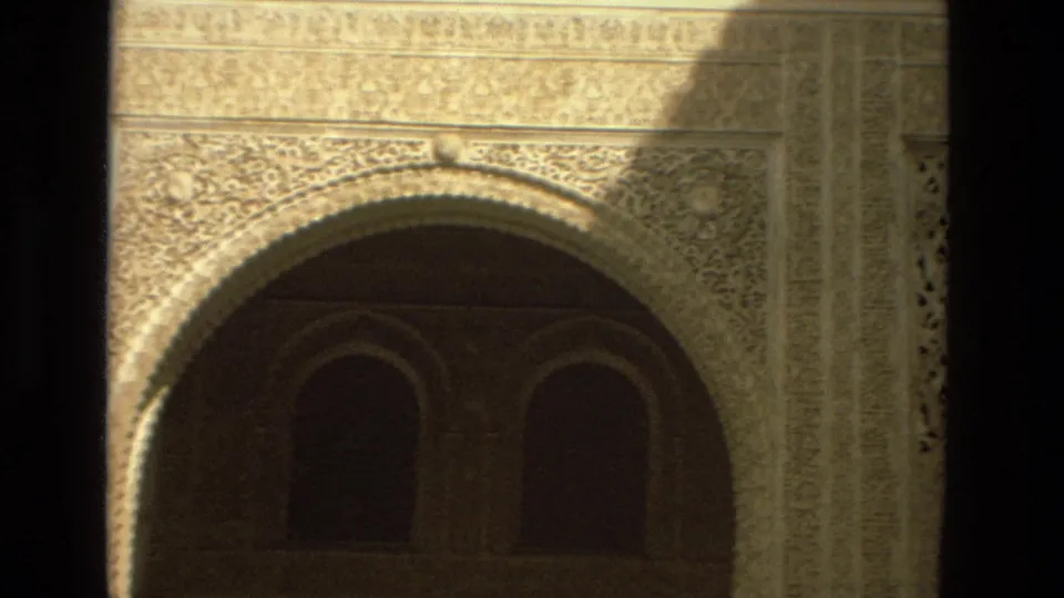 1978 Córdoba frame showing a large carved horseshoe arch facade with shadowed interior arches and sunlit stone ornament.