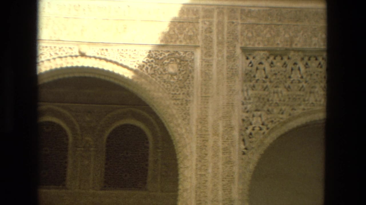 1978 8mm frame from Córdoba, Spain showing carved Moorish-style arches, lattice-like wall detail, and shadowed window openings.