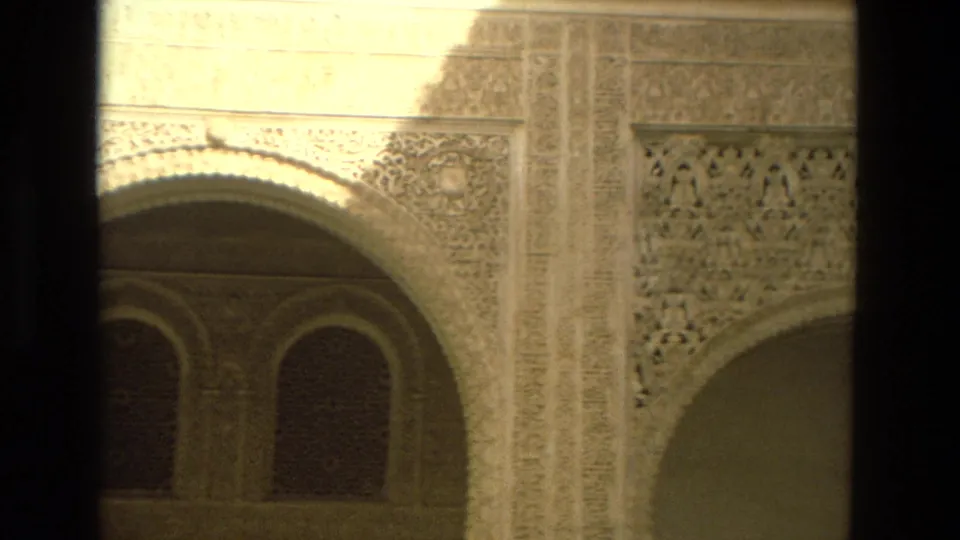 1978 8mm frame from Córdoba, Spain showing carved Moorish-style arches, lattice-like wall detail, and shadowed window openings.