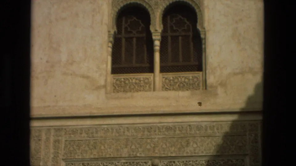 1978 Córdoba travel frame showing paired arched windows, geometric grilles, and a horizontal band of carved architectural detail.