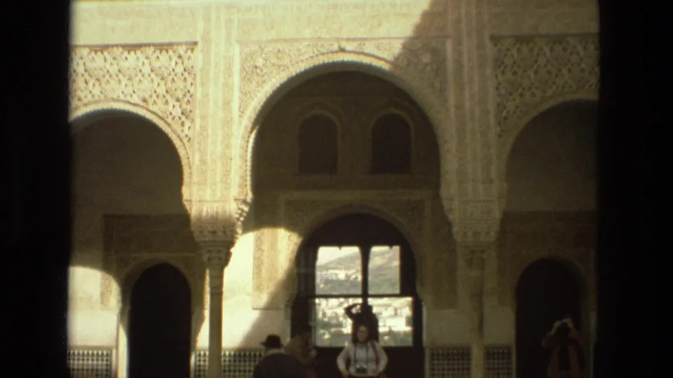 1978 Córdoba courtyard frame showing ornate arches, a bright exterior opening, and visitors walking below the architecture.
