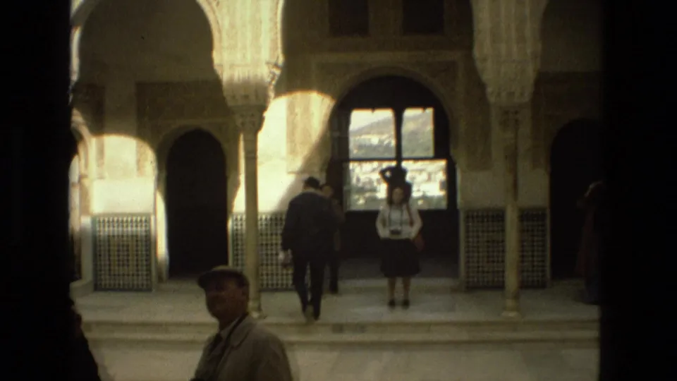 1978 Córdoba travel footage shows tourists in period clothing under arches, with tiled wall panels and bright courtyard light beyond.