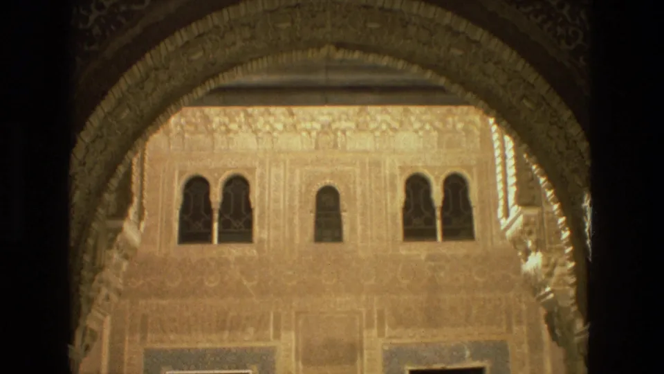 An ornate Moorish-style arch frames a sunlit Córdoba courtyard wall with carved surface detail and small arched windows.