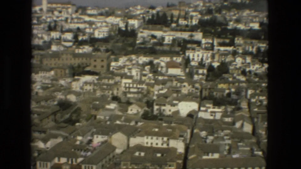 Vintage 8mm frame of a Spanish hillside city panorama, with clustered rooftops, white walls, and dark trees.
