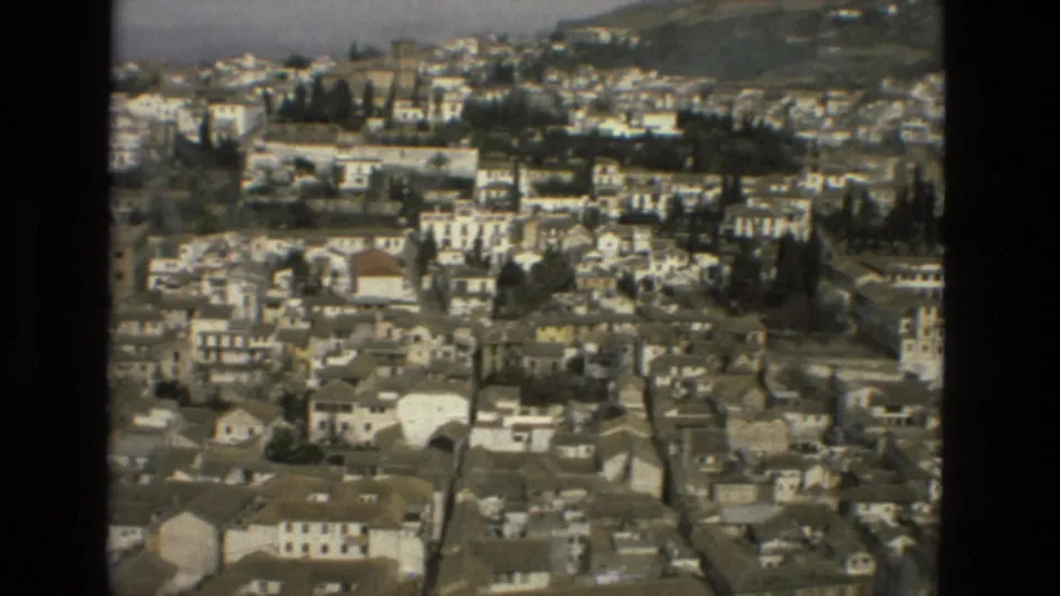 1978 8mm view over Córdoba, Spain, showing dense white buildings, rooftops, trees, and a hill rising behind the city.