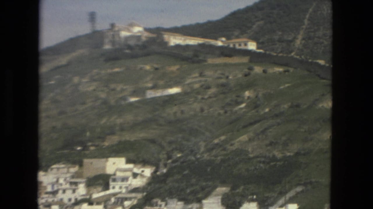 White buildings on a green hillside with a larger structure near the ridge.