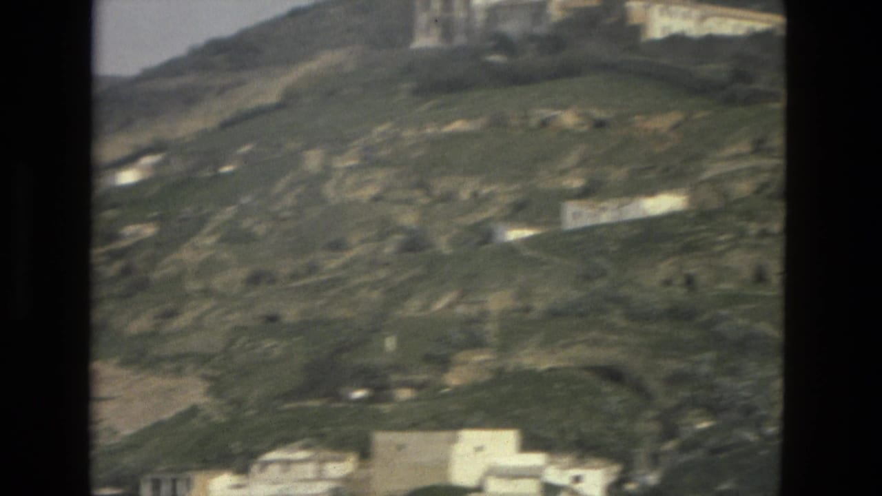 Soft 8mm frame from Córdoba, Spain, showing scattered white structures, hillside tracks, and open green-brown terrain.