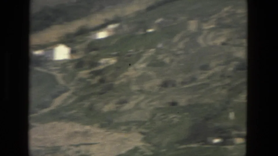 Motion-blurred 1978 8mm frame of the Córdoba-area hillside, with pale buildings, fields, and rough tracks crossing the slope.