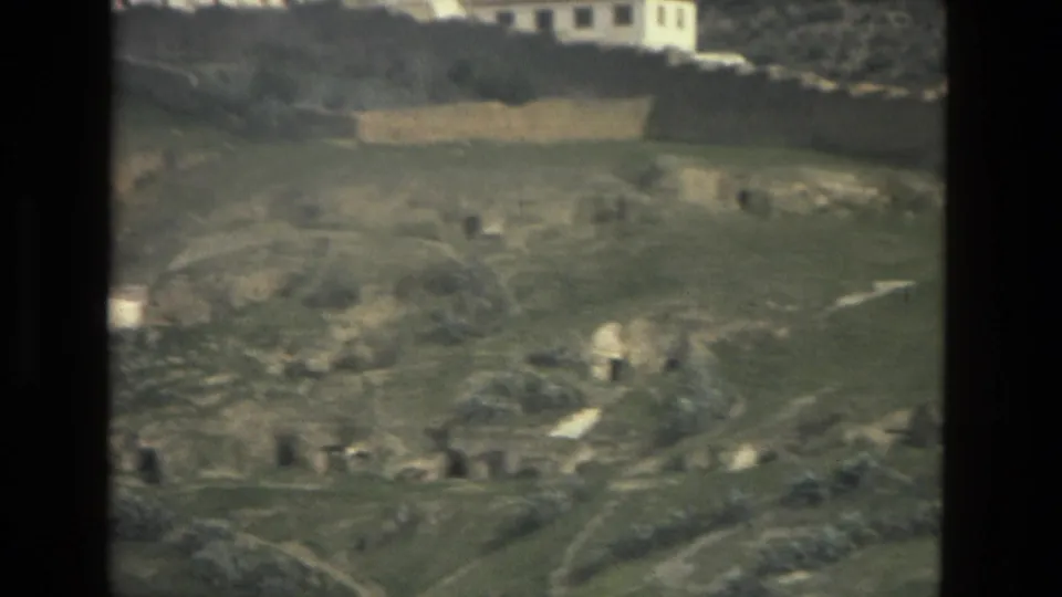 1978 8mm view of a Córdoba hillside with white buildings at the slope edge, rocky ground, and terraced paths in open land.
