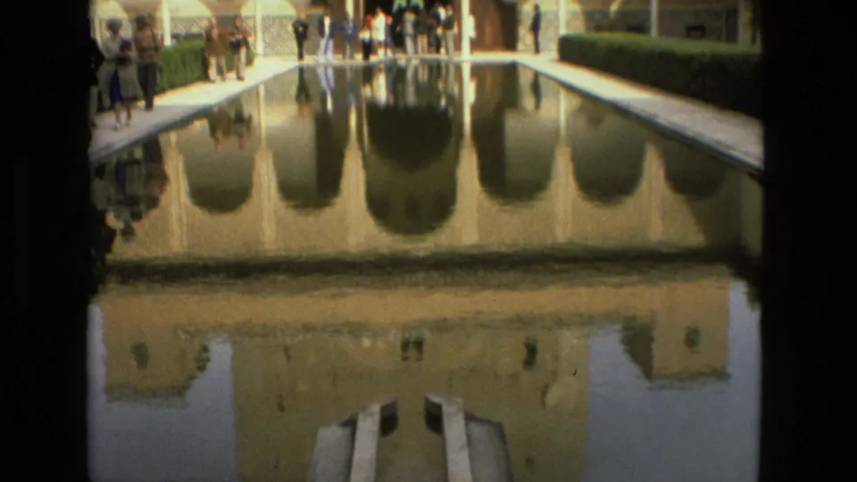 The Alcázar of Córdoba courtyard pool reflects the tower and arches while tourists stand along the walkways.