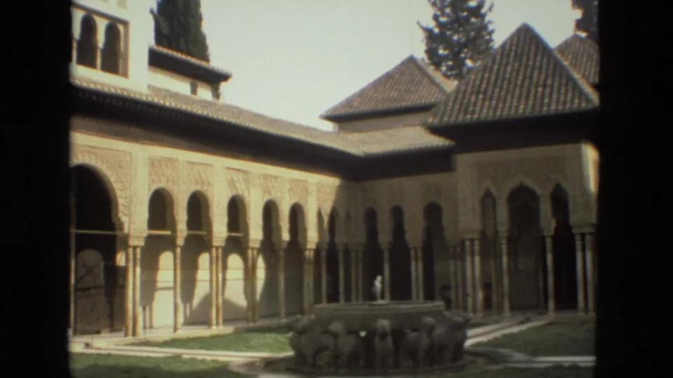 1978 8mm courtyard view in Cordoba, Spain, with arched facade, tiled roofs and stone lion fountain.