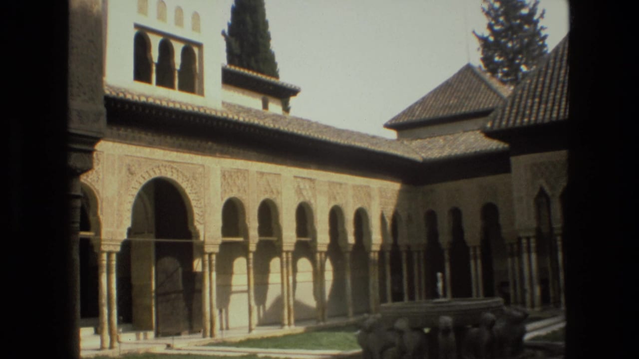Sunlit courtyard with arched colonnades, tiled roofs, carved walls, a low fountain area, and dark trees.