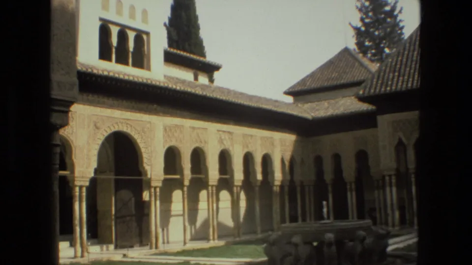 1978 8mm view in Córdoba, Spain, showing a sunlit historic courtyard with arches, carved wall surfaces, tiled roofs, and a low fountain area.