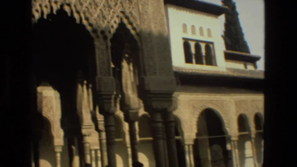 Córdoba, Spain travel-film frame showing a shadowed ornate archway and columns beside sunlit carved walls and upper arched windows.