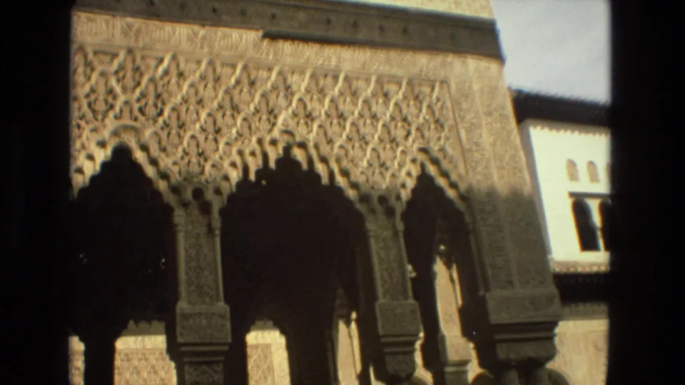 1978 Córdoba home-movie frame focused on dense Moorish-style carved arches and columns, with a pale wall and small arched windows behind.