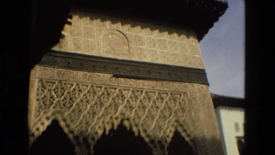 Angled 8mm frame from Córdoba, Spain, showing detailed carved wall ornament over dark arched openings, with pale architecture and sky nearby.