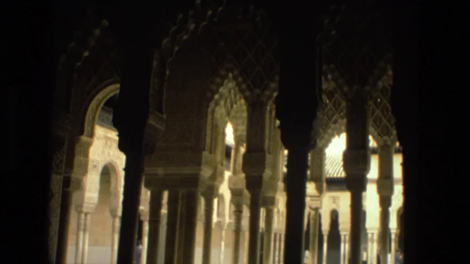Shadowed 1978 Córdoba arcade view through patterned Moorish-style arches toward columns and a bright courtyard outside.