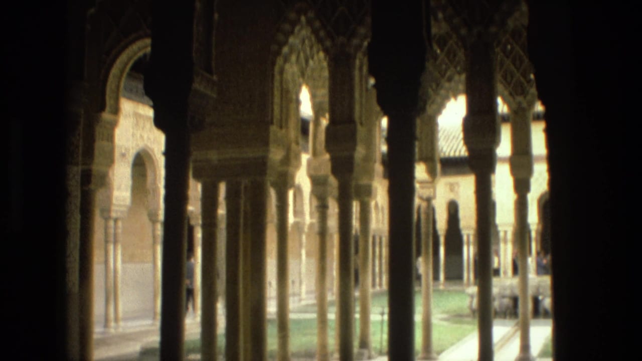 Dark colonnade framing arched courtyard openings and a sunlit garden beyond.