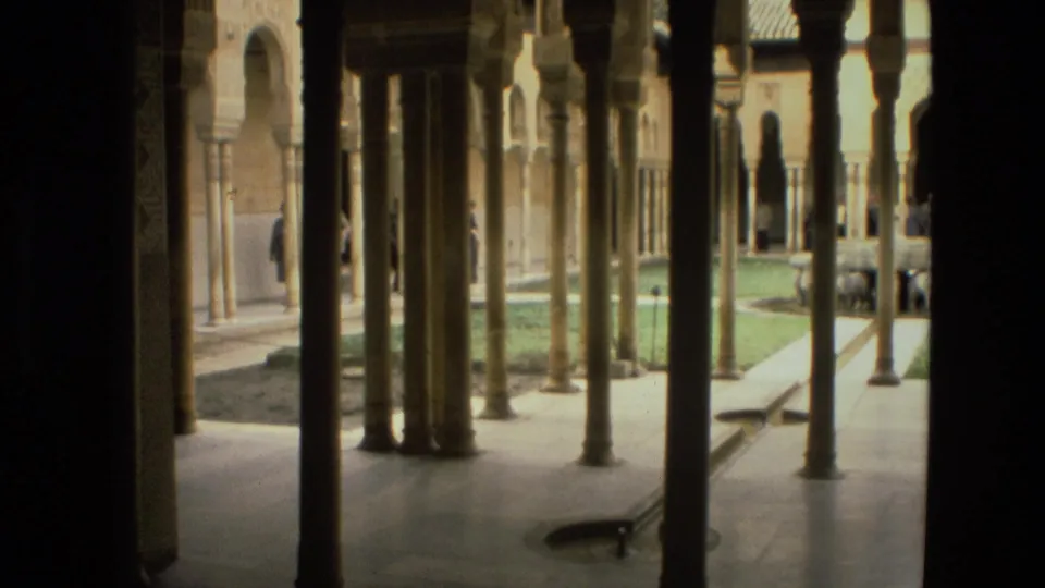 Cordoba courtyard scene from 1978 8mm footage, with slender columns, arched walls, garden edges, and distant visitors.
