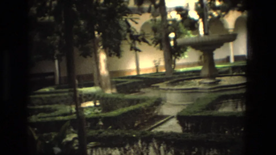 1978 8mm Cordoba garden view with hedges, trees, a fountain, a curving path, and blurred visitors in the background.