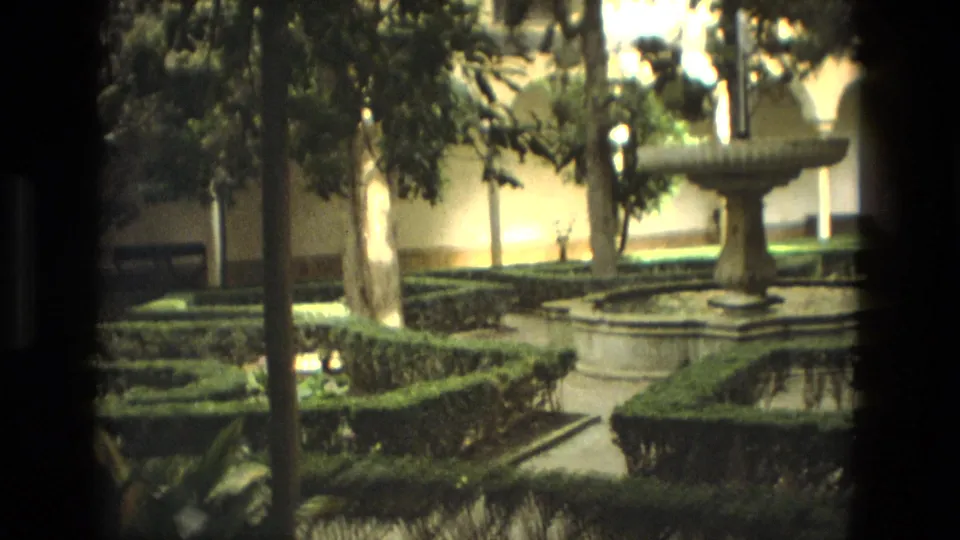 1978 Córdoba frame with a stone fountain, formal hedges, shaded trees, and arched courtyard architecture.