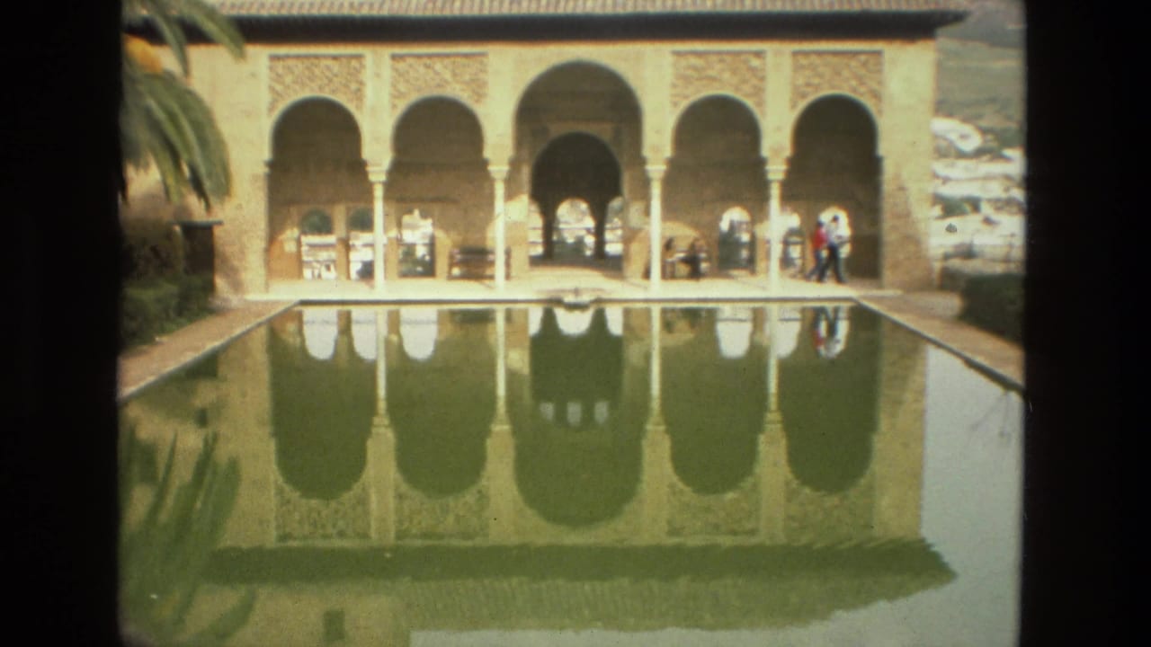 Arched building reflected in a long pool with visitors on the walkway.