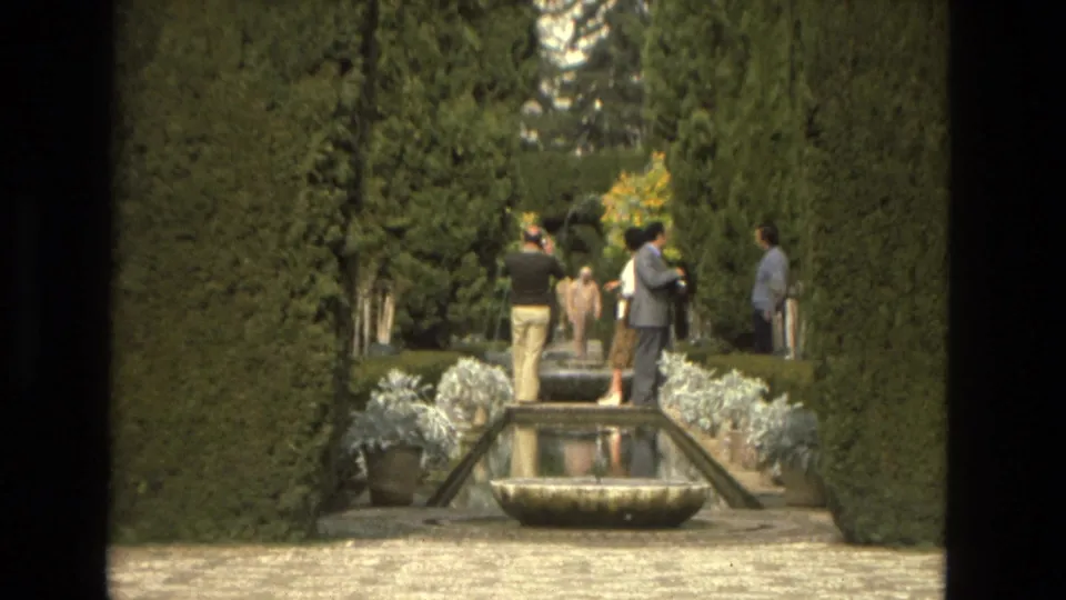 1978 Cordoba garden view with tall hedges, a central water channel, fountain basin, and distant visitors on the path.