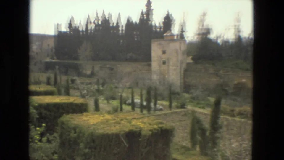 1978 Cordoba garden view with clipped hedges, cypress trees, old stone walls, and a square tower at the edge of the grounds.