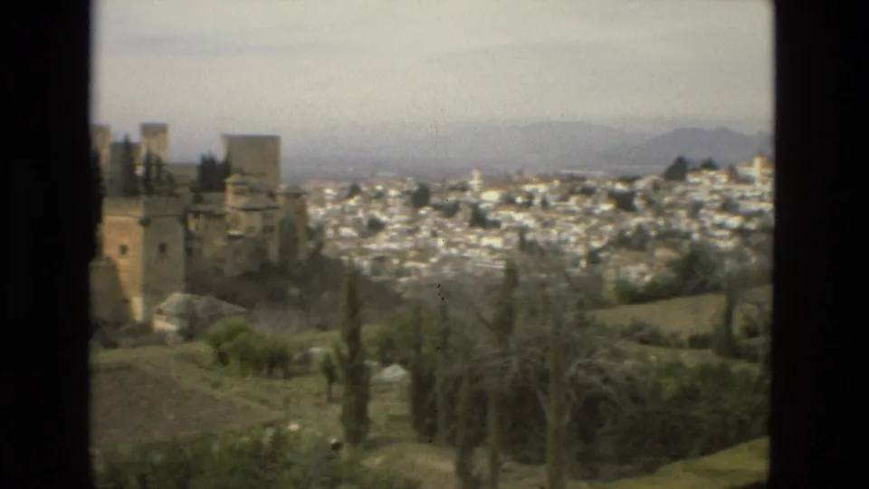 1978 home-movie frame of Córdoba’s white old-town buildings beyond garden paths, stone walls, and foreground trees.