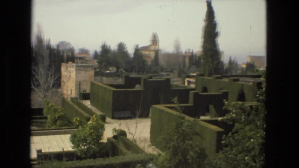 Elevated 1978 Córdoba garden view showing formal hedges, paths, trees, stone structures, and distant historic towers.