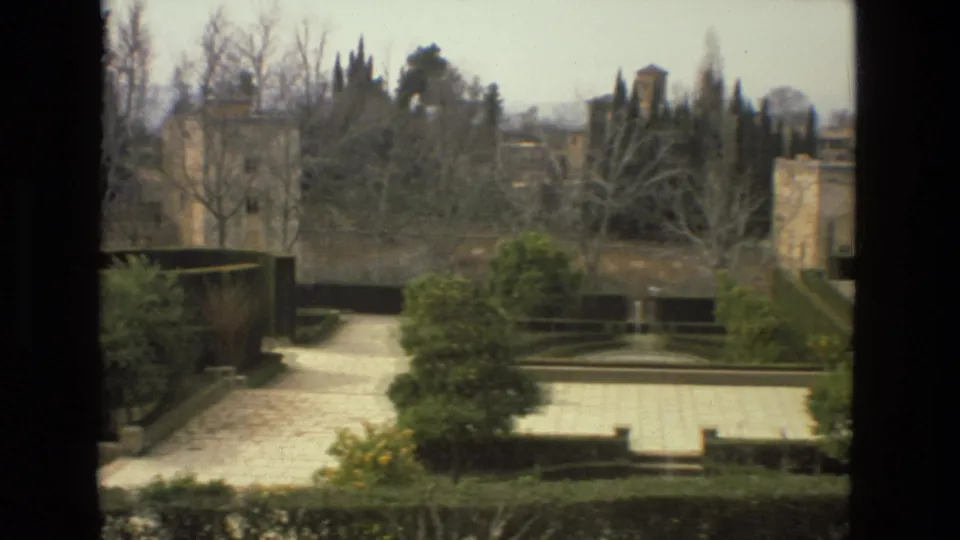 1978 Córdoba garden view showing a stone path, formal hedges, bare and evergreen trees, garden walls, and distant towers.